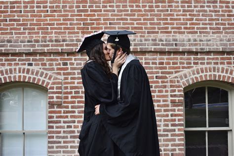Two People In Graduation Gowns Standing Next To Each Other And One Is Kissing The Other