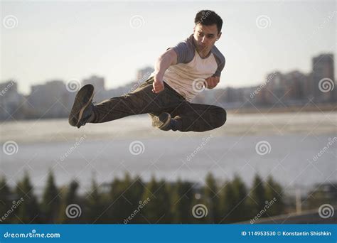 Young Man Fighter Performs Flying Kick In Front Of Skyline Stock Photo