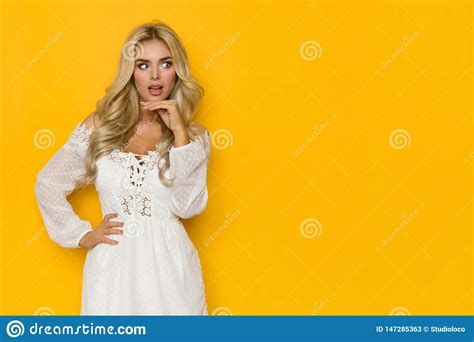 Surprised Beautiful Blond Woman In White Dress Is Hand On Chin And