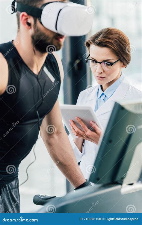 Sportsman Running On Treadmill Near Attractive Doctor During Endurance
