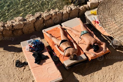 Two Girls In Bikinis Sunbathing On Sun Loungers Against The Backdrop Of