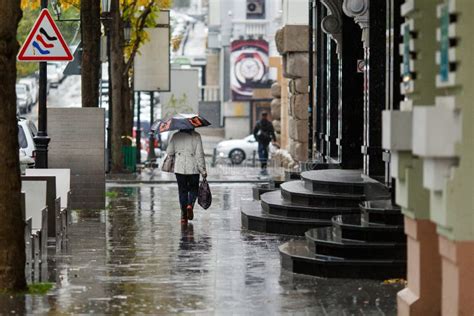 People Walk Under Umbrellas During Light Rain On The Wet Streets Of The