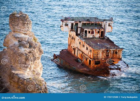 Sunken Rusty Cargo Ship In Still Blue Sea Waters With Rocks Around