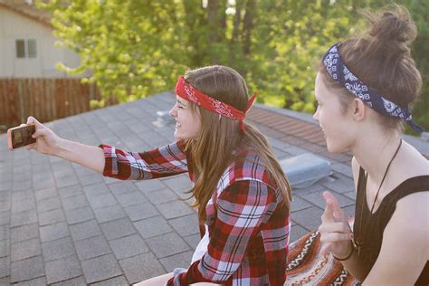 Teen Girls Take Selfies With Phone While Sitting On Roof Top By
