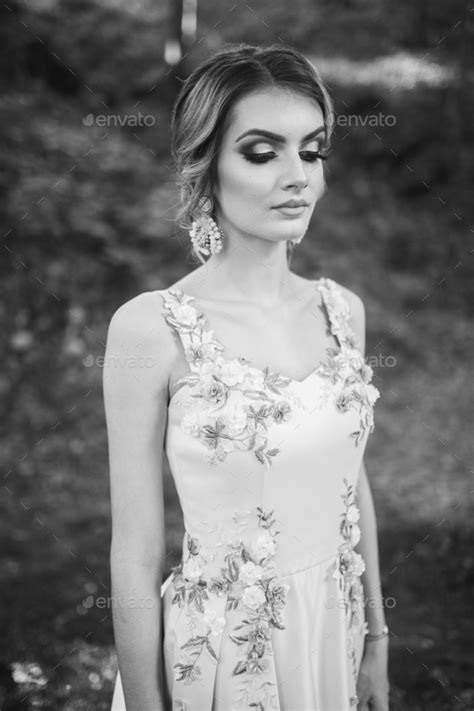 grayscale of a gorgeous blonde female in an elegant yellow dress looking dow in a park stock