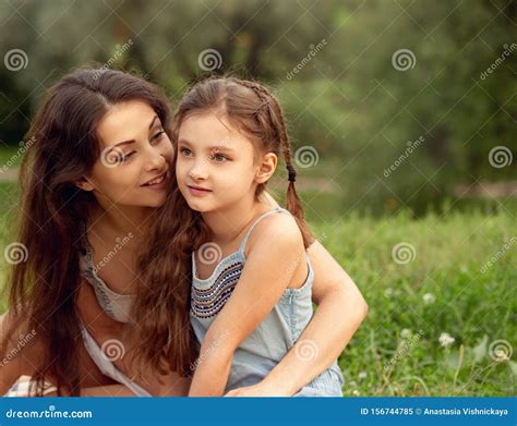 Beautiful Young Mother Embracing Her Cute Long Hair Daughter On Summer Green Grass Background In