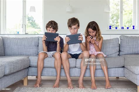 Brothers And Sister On Sofa With Digital Tablets And Mobile High Res