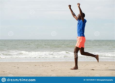 Side Portrait Of Happy Young Man Running At Beach With Arms Raised
