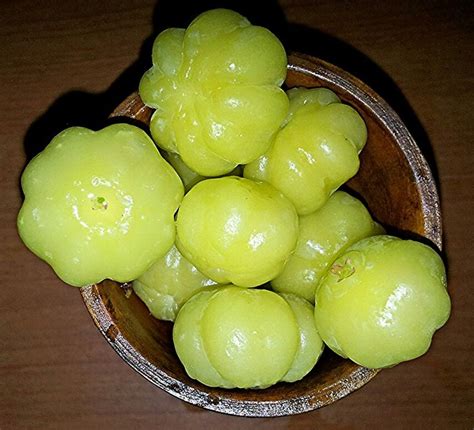 A Wooden Bowl Filled With Green Fruit On Top Of A Table