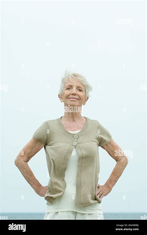 Senior Woman Standing With Hands On Hips Smiling At Camera Ocean Horizon In Background