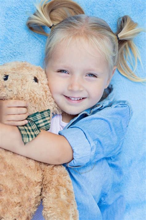 Cute Little Girl With Blonde Hair Lying On The Bed With Stuffed Teddy