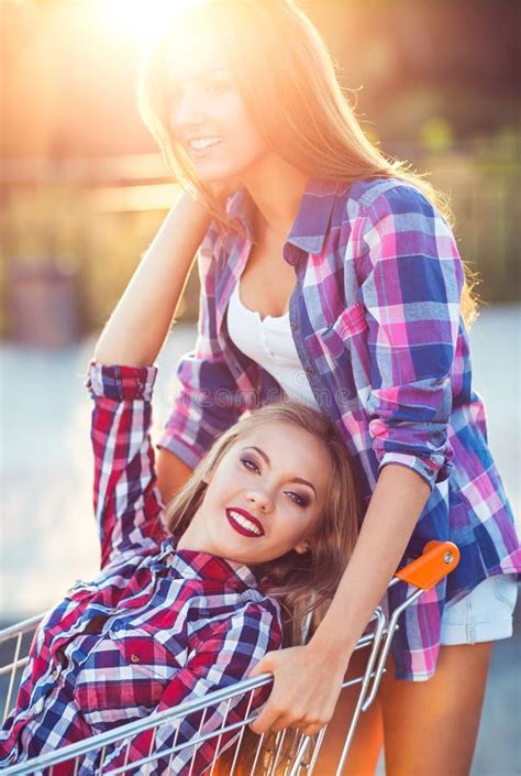 Two Happy Beautiful Teen Girls Driving Shopping Cart Outdoors Stock