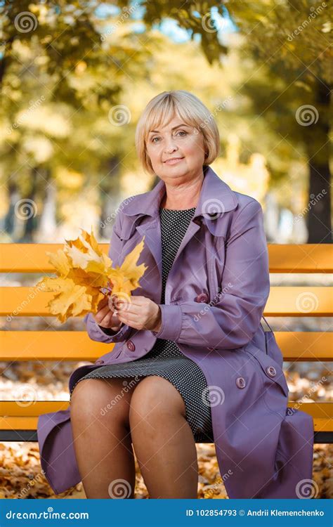 a mature woman sits on a bench in the park and holds autumn leaves stock image image of older