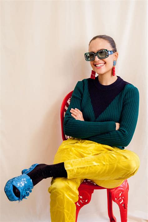 A Woman Sitting On A Red Chair With Her Arms Crossed Wearing Sunglasses And Yellow Pants