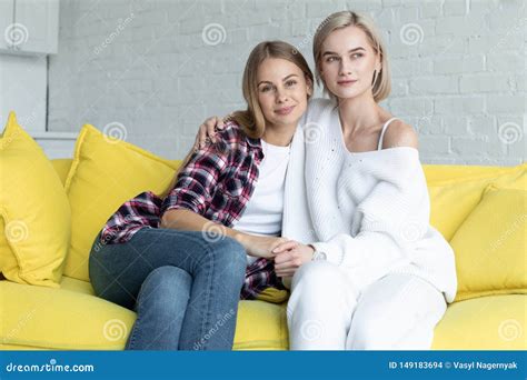 portrait of beautiful lesbian couple in casual clothes that hugging sitting on yellow sofa at
