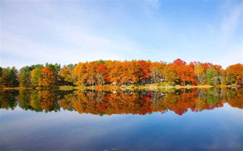 A Lake Surrounded By Lots Of Trees With Fall Foliage On Its Sides And
