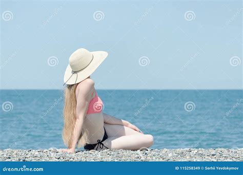 Beautiful Girl In A Swimsuit And Hat Sits On A Beach On A Background Of