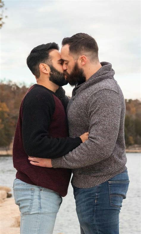 Two Men Standing Next To Each Other With Their Arms Around One Another And Kissing The Other
