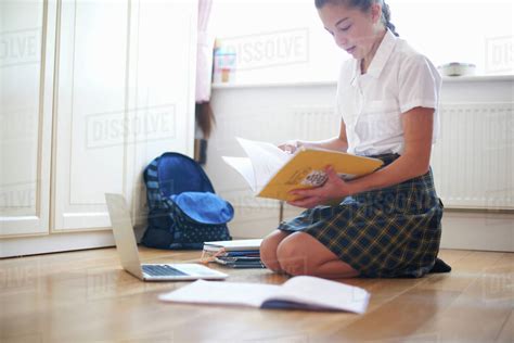 Teenage Schoolgirl Kneeling On Floor Looking At Book Stock Photo
