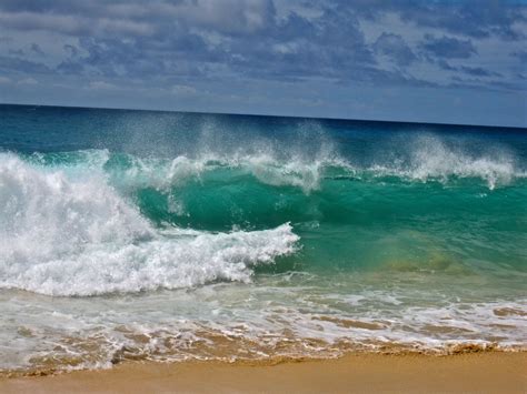 An Ocean Wave Breaking On The Beach With Blue Sky And Clouds In The
