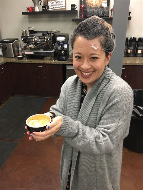 A Woman Holding A Cup Of Coffee In Her Hand And Smiling At The Camera While Standing Next To A