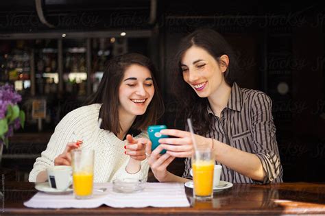 Two Beautiful Girls Having Fun In A Bar Looking At Mobile Phone By Stocksy Contributor Mak