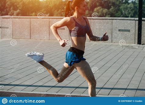 Smiling Athletic Woman Running Fast Outdoors Next To Pavement Sidewalk