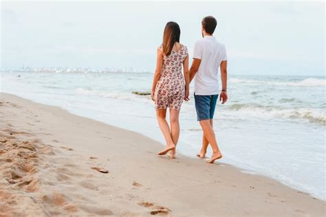 Back View Of Happy Young Couple Walking On A Deserted Tropical Beach