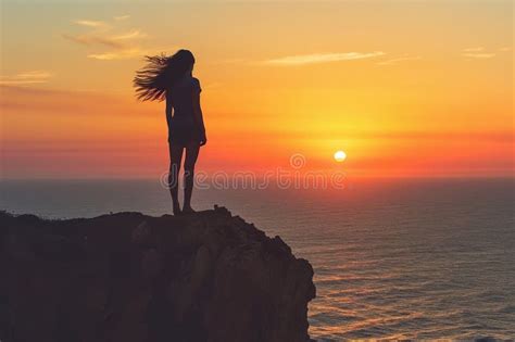 Girl Standing On A Cliff Looking Out At The Sunset With Her Hair Blowing In The Wind Stock