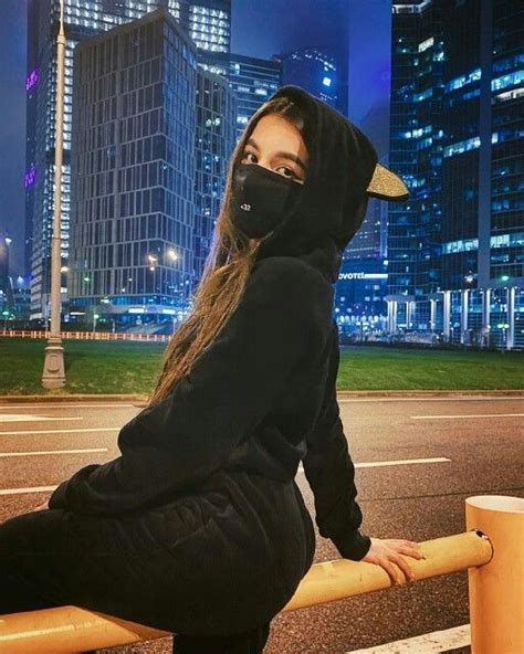 A Woman In A Black Hoodie Leaning On A Rail With Her Face Covered By A Mask