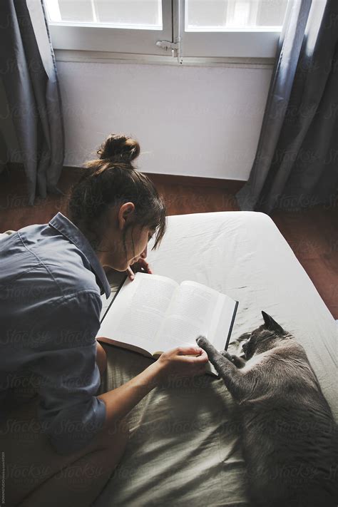 Young Casual Woman And Her Cat Lying On The Bed With Coffe Reading A Book By Stocksy