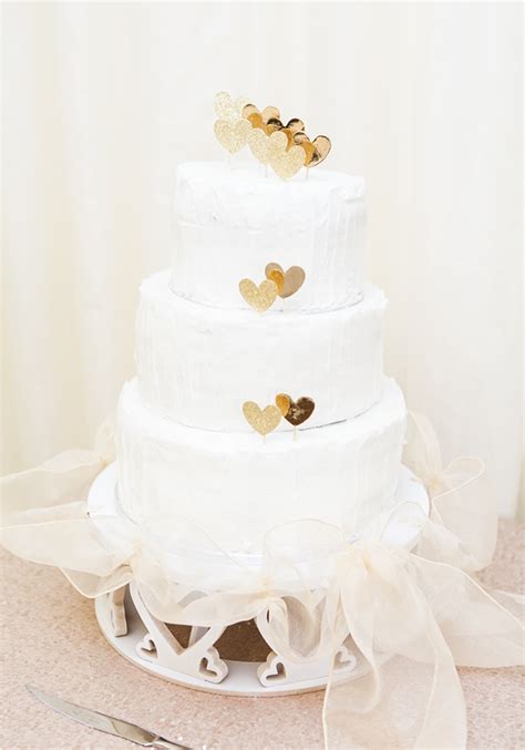 A White Wedding Cake With Gold Hearts On Top