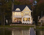 a white house sitting on top of a lake next to a dock with lights on