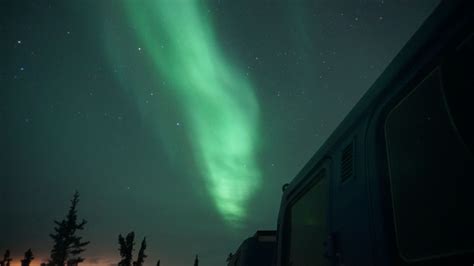 An Aurora Bore Is Seen In The Night Sky Above A Camper Trailer And Trees