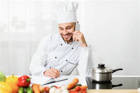 Chef Man Talking On Phone Taking Notes Standing In Kitchen Stock Image