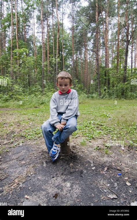 Young Boy Sitting Alone On Tree Stump In Forest Play In The Forest