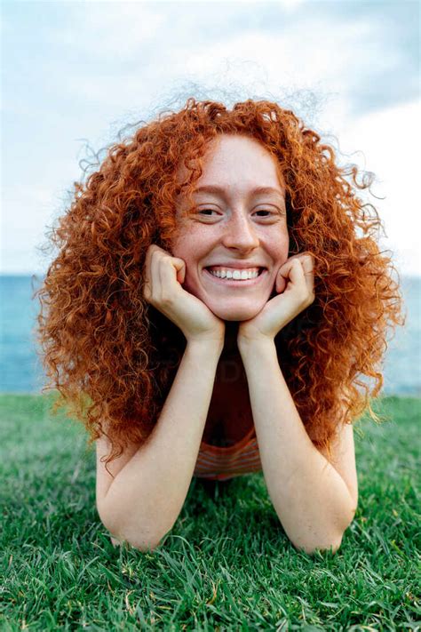 Happy Curly Redhead Haired Female With Freckles Lying On Lawn Looking