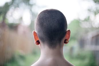 A Girl With A Shaved Head And Red Bushes In The Background Stocksy United
