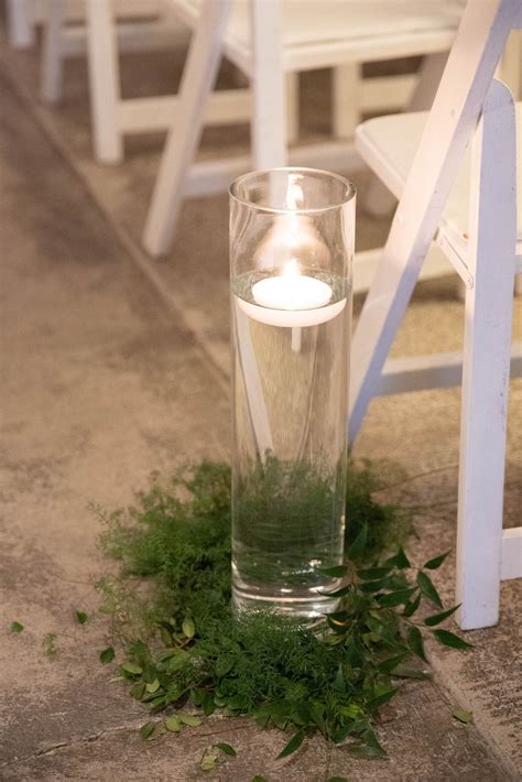 Floating Candle Surrounded By Greenery Placed Along The Aisle Pews