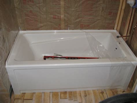 A worker uses a level and tape measure to measure the front of the new tub. Installing Maax Advanta "New Town" Bath Tub, Leveling And ...