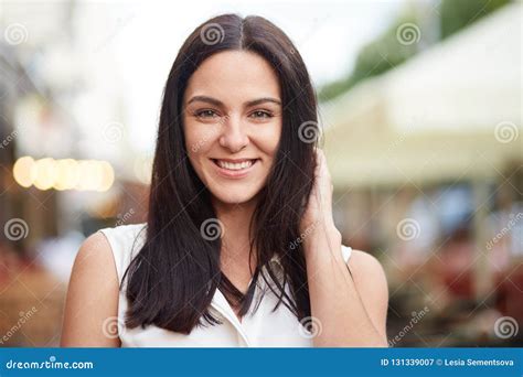 Headshot Of Pleased Brunette Female Looks Happily At Camera Poses Outdoor Enjoys Spare Time