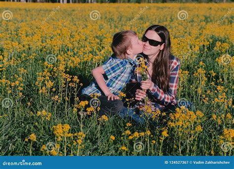 Boy Gives His Mother A Bouquet Of Wild Flowers And Kisses Her Sitting
