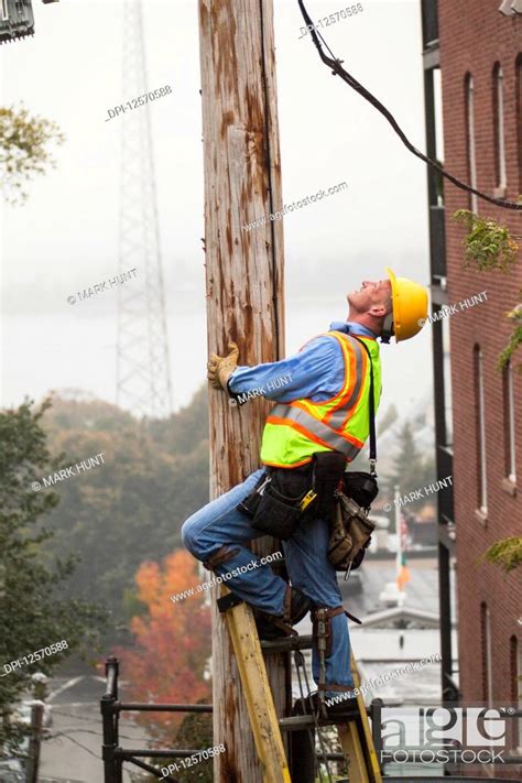 Cable Lineman Climbing Up A Ladder On City Power Pole Stock Photo
