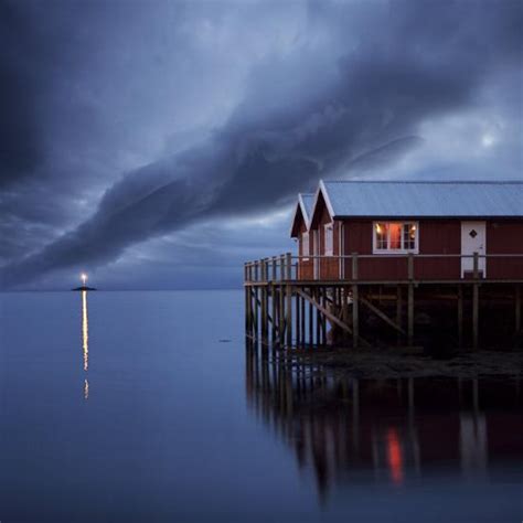 Rorbuer On Stilts At Dusk With Lighthouse Lofoten Islands Norway