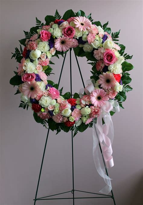 A Floral Wreath With Pink White And Green Flowers On A Metal Easel