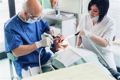 Dentist And Dental Nurse Carrying Out Procedure On Male Patient Stock