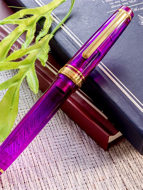 A Purple Pen Sitting On Top Of A Book Next To A Plant