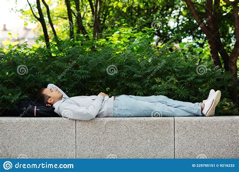 Carefree Man Traveler Sleep On Backpack Outdoors In Urban Park Guy In