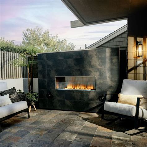 An Outdoor Fireplace In The Middle Of A Patio With Two Chairs And A