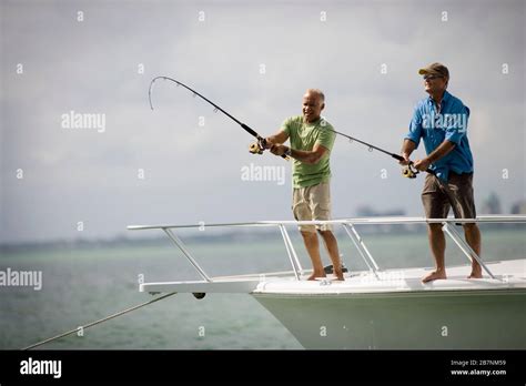 Two Smiling Mature Men Fishing Off The Edge Of A Boat Together In The